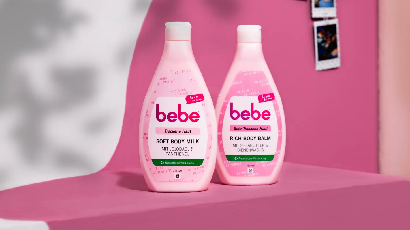 Bebe Produkte Soft Body Milk und Rich Body Balm stehen aufgereiht vor pinkem Hintergrund.