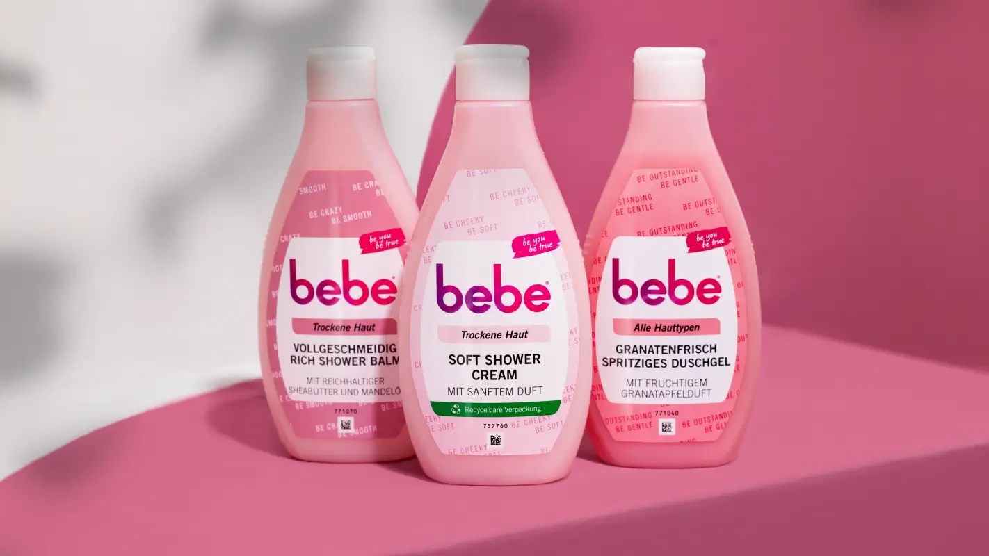 Bebe Produkte Rich Shower Balm, Soft Shower Cream und Spritziges Duschgel stehen aufgereiht vor pinkem Hintergrund.