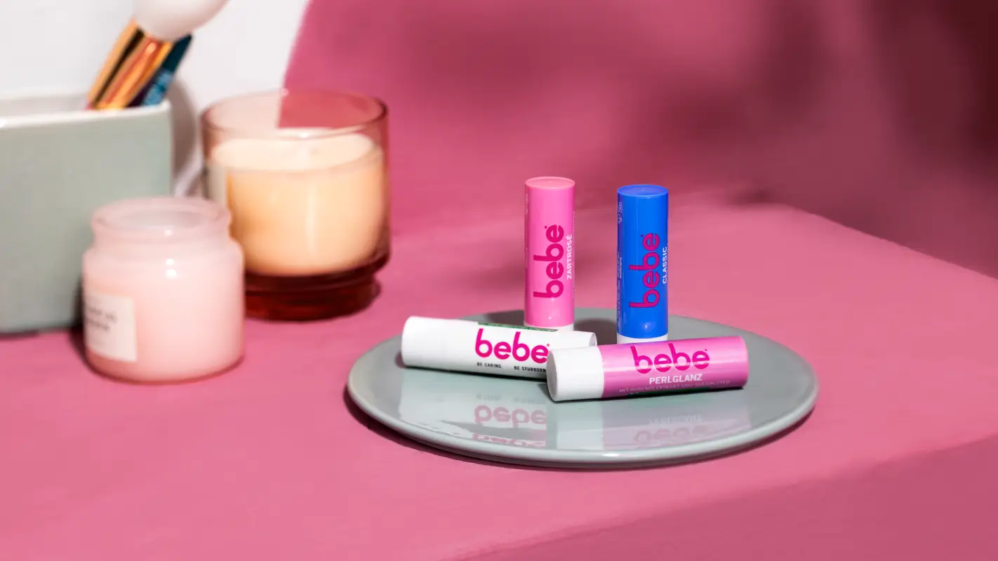 Bebe Lippenpflegestifte liegen auf einem Tablett vor pinkem Hintergrund.
